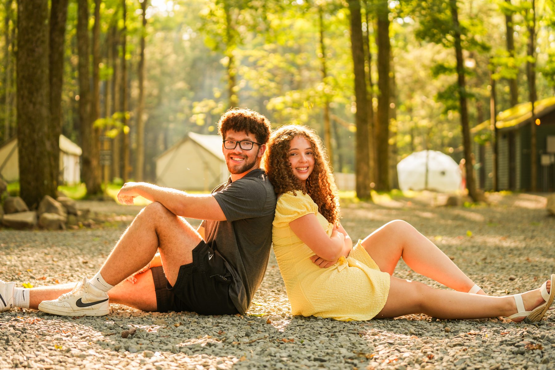 Senior portrait of a couple sitting back to back in golden hour light in a forest in Western Massachusetts